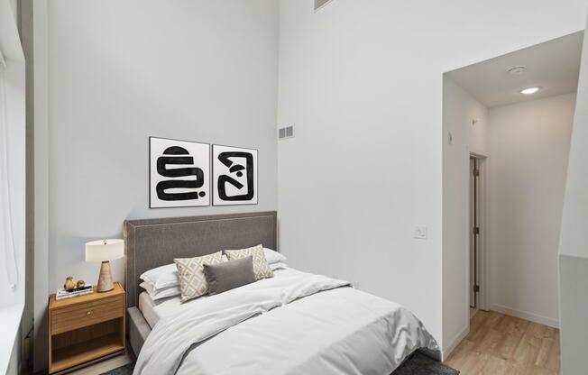 Cozy bedroom setting with a gray upholstered bed, black and white wall art, and bedside tables with lamps, emphasizing a minimalist aesthetic.