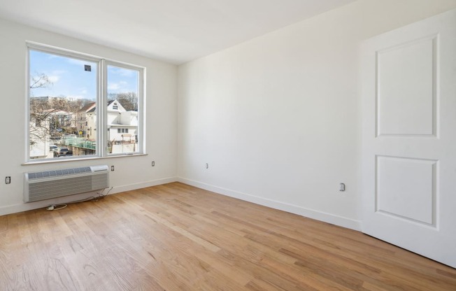 an empty living room with a large window and wooden floors