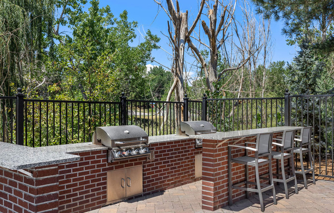 a brick outdoor kitchen with two bbqs and a table with chairs at Arcadia Apartments, Centennial