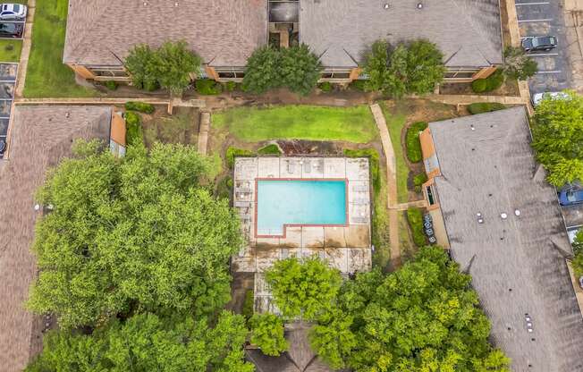 An aerial view of a pool surrounded by trees and buildings.