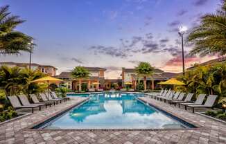 a swimming pool with lounge chairs around it at sunset