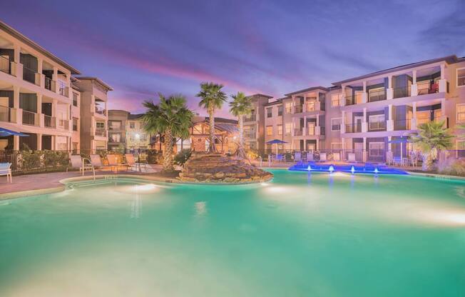 A swimming pool in front of a building with lights on.