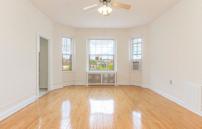 an empty living room with a ceiling fan, hardowod flooring  and three windows at the calverton apartments in washington dc