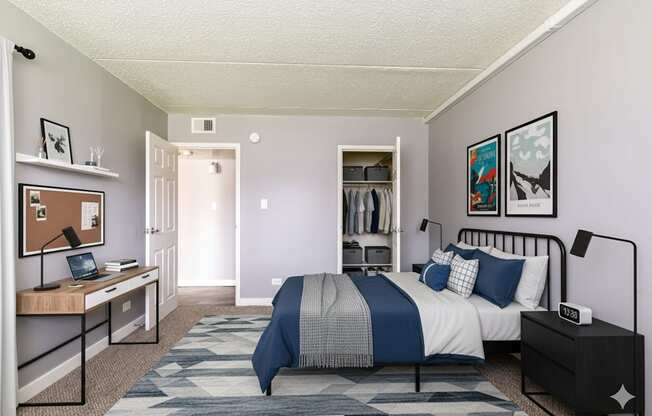 A bedroom with a bed, nightstand, and a desk with a computer.