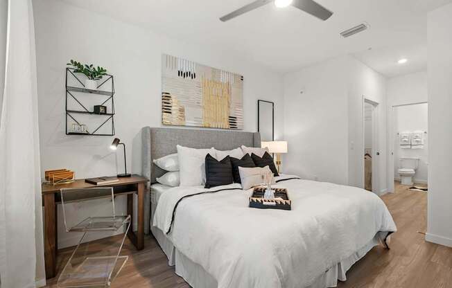 A bedroom with a bed, desk, chair, and a ceiling fan.