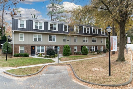 the front of an apartment building with a driveway and trees