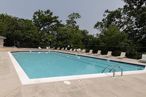 A large outdoor swimming pool surrounded by trees and lounge chairs.