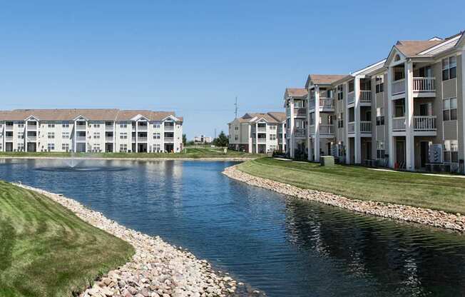 A river runs through a grassy area next to apartment buildings.