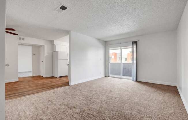 A spacious room with a carpeted floor and a sliding glass door leading to a balcony.