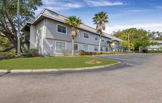 A building with a grey roof and white walls is surrounded by palm trees.