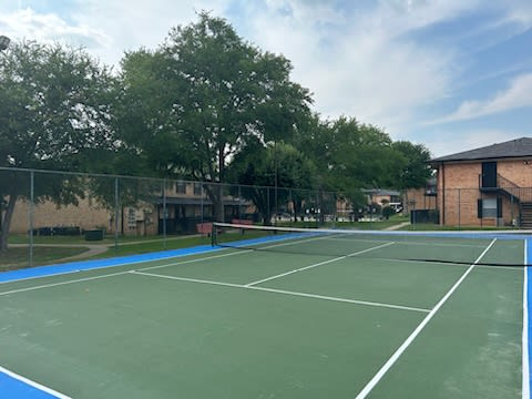 a tennis court in front of a building with trees