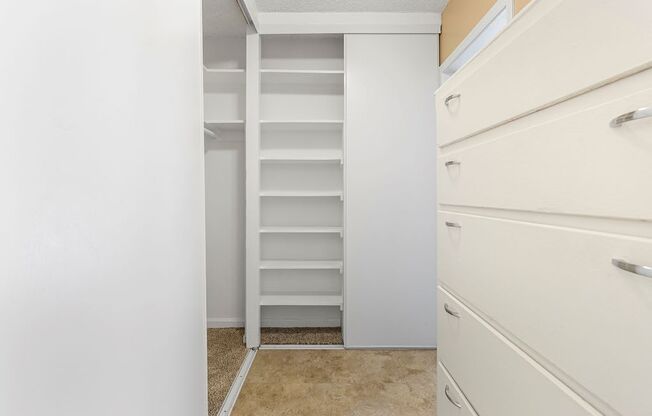 a walk in closet with white walls and a white dresser next to it