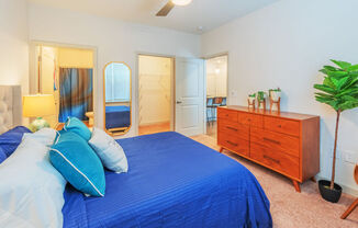 A bedroom with a blue bedspread and a wooden dresser.
