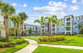 Sidewalk surrounded by luscious green landscape and palm trees at Dunedin Commons apartments in Dunedin, FL