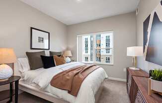 A bedroom with a large bed and a window showing a cityscape.