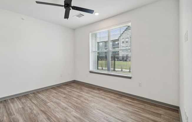 the living room of an empty apartment with wood flooring and a window at The Depot in The Depot Raymore, MO 64083