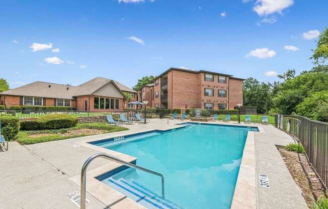 A swimming pool surrounded by a concrete patio and a brick building.