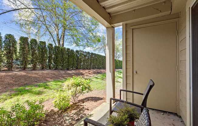 A chair sits on a porch with a view of a tree-lined field.