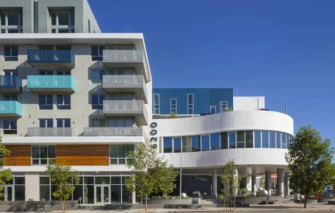 Woodland Hills Apartments- The Q Variel - Side View of the Building Exterior with White, Blue, and Grey Walls, Private Balconies, Trees, and Modern Designs