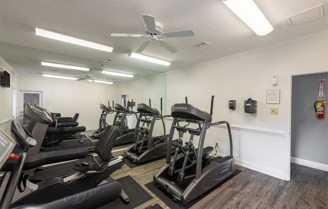 a gym with cardio machines and a ceiling fan