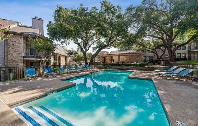 A swimming pool surrounded by trees and chairs.