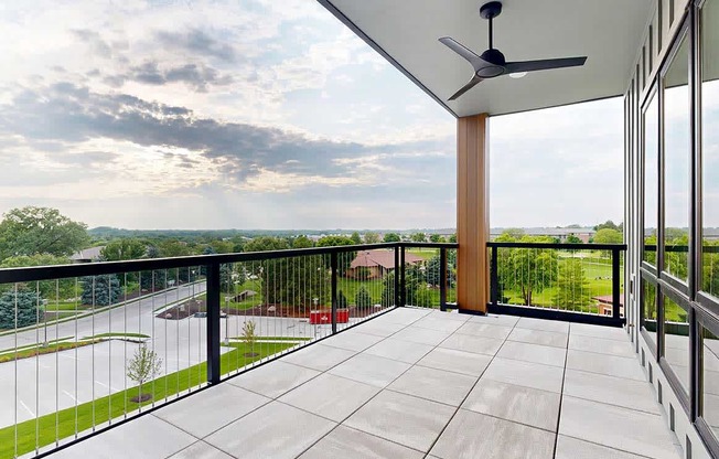 An oversized balcony with a metal and wire railing, stone tile flooring, a ceiling fan, and a corner view of the neighborhood.