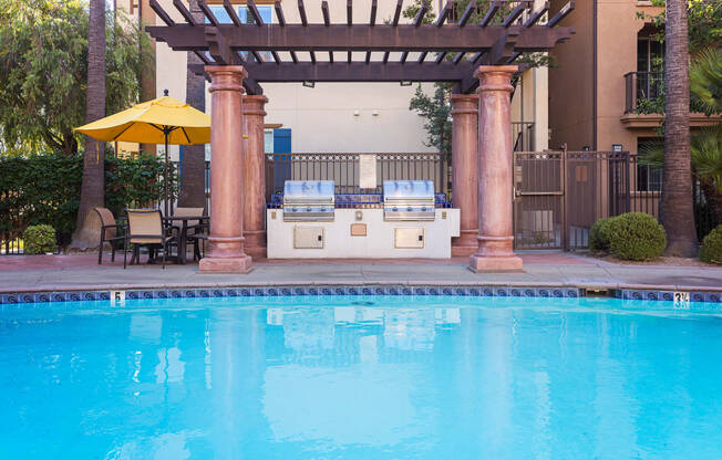 an outdoor kitchen next to a swimming pool with a hot tub and a pergola