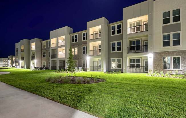 Apartment complex with green lawn and lights on.