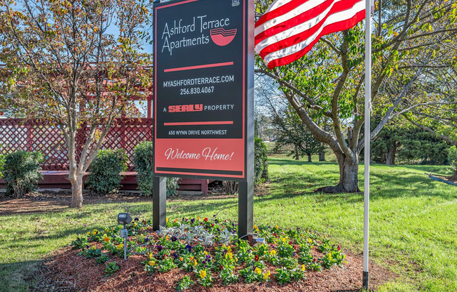 A sign for Ackford Terrace Apartments is in front of a tree and an American flag.