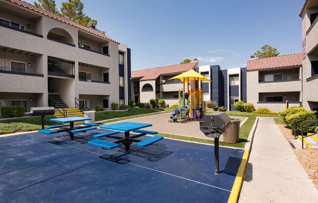 an outdoor play area with picnic tables and an umbrella