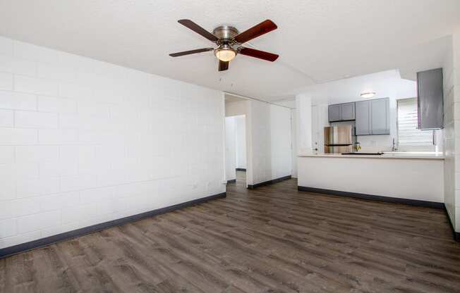 an empty living room with a ceiling fan and a kitchen at Palms of Kilani Apartments, Wahiawa, HI, 96786