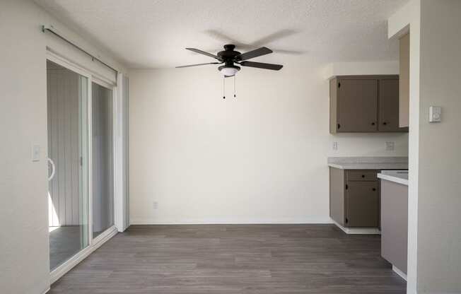 an empty living room with a ceiling fan and a kitchen