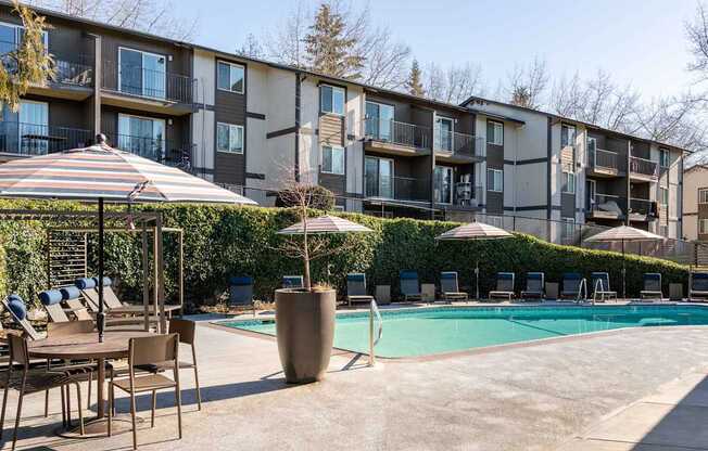 A pool area with chairs and umbrellas in front of apartment buildings.