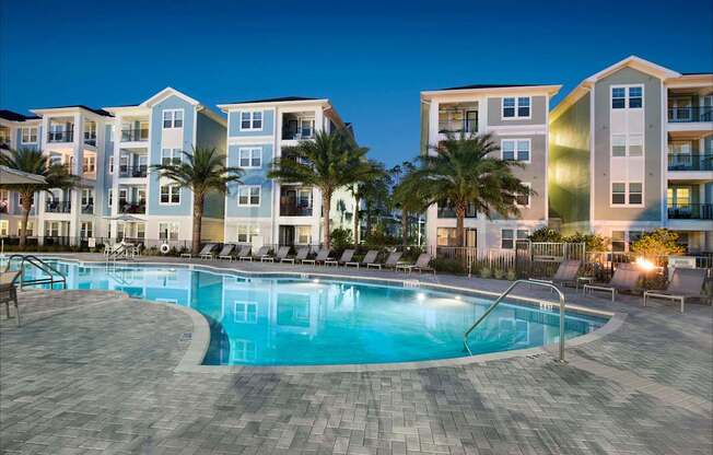 A swimming pool in front of apartment buildings at dusk.