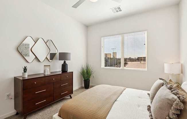 A bedroom with a bed, dresser, and a window with blinds.