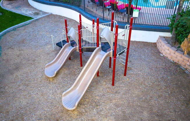 Two slides in a playground with red poles.