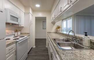 Kitchen with white cabinets and white appliances and large pass-through window in a 2 bedroom, 1.5 bath 1084 sq ft, 2-floor townhome at The Biltmore Apartments located in the Vickery Midtown neighborhood of Dallas, TX.