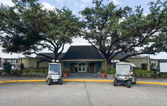 Two golf carts are parked in front of a building with a large tree in the background at Willow Creek Apartments, Texas