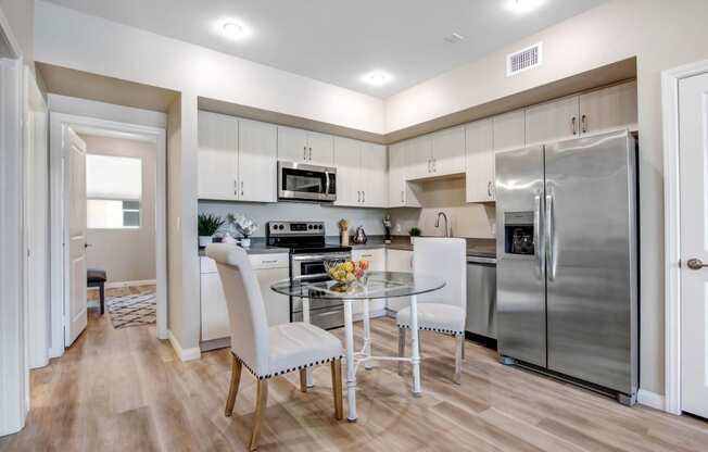 a kitchen with white cabinets and stainless steel appliances and a glass table with white chairs