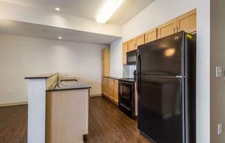 A kitchen with a black refrigerator and wooden cabinets.