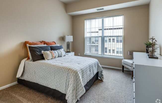 a bedroom with a bed, dresser and a large window