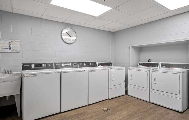 a laundry room with white washers and dryers and a clock on the wall