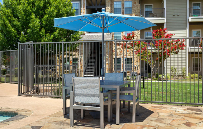a table and chairs under an umbrella in front of a pool