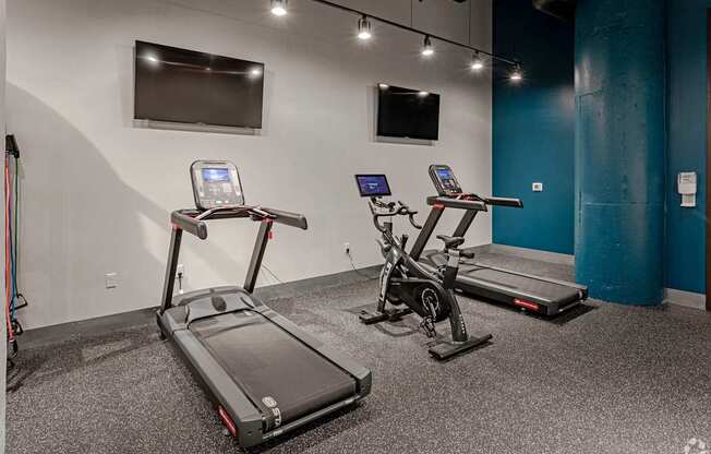 Two treadmills are in a room with a blue wall and a television.