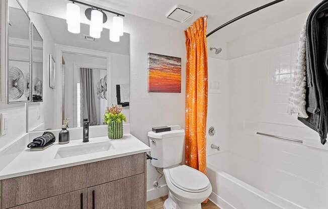 A bathroom with a white toilet, sink, and orange curtain.