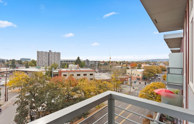 A balcony overlooks a city street with buildings and trees.