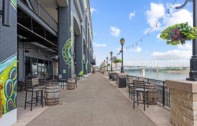 a sidewalk with tables and chairs near a river and a bridge