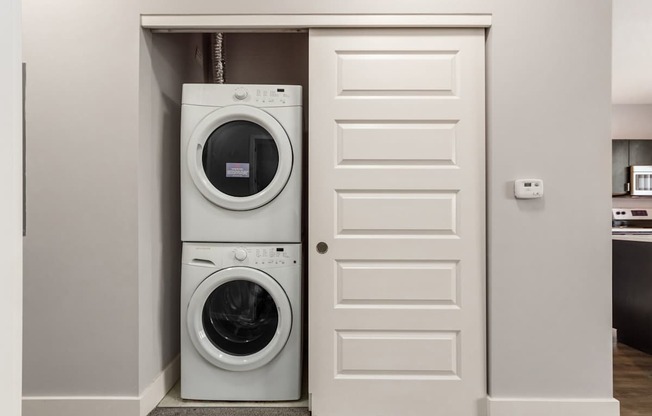 A white door is open to reveal a stacked washer and dryer.