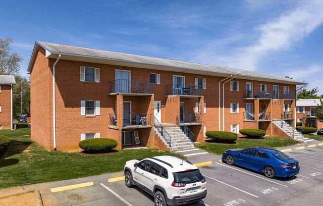 A white car is parked in a parking lot in front of a red brick apartment building.