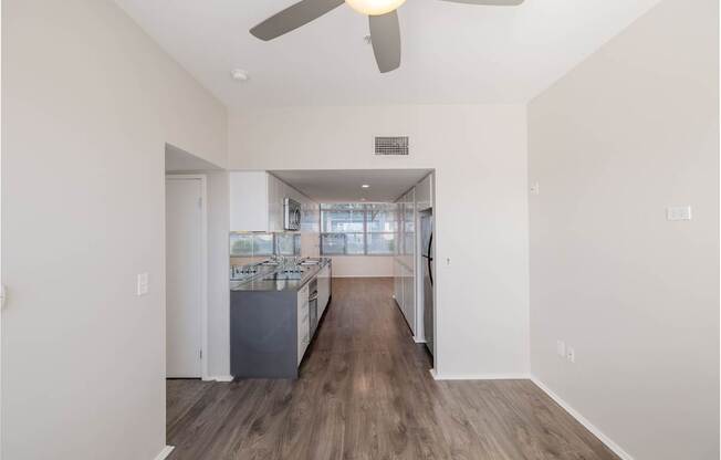 A spacious room with a ceiling fan and a kitchen area in the background.